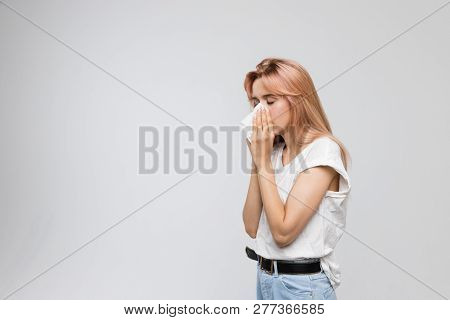 Portrait of cute young woman blowing her nose into a paper napkin, closed eyes/cold, sneezing, allergy symptoms, flu, rhinitis, sickness, desperately sick, healthcare and medicine concept/copy space.