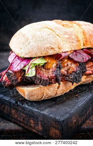 Traditional barbecue pulled pork piece of Bosten butt as sandwich with lettuce as closeup on a black board 