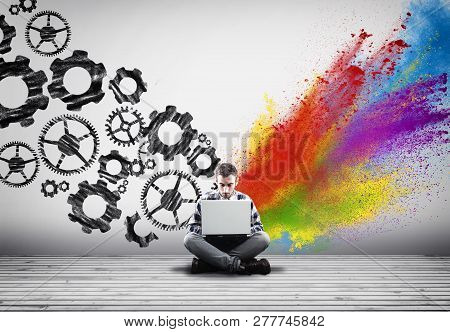 Man Working On Laptop Against An Wall Painted With Engine Gear Wheels And Powder Explosion.