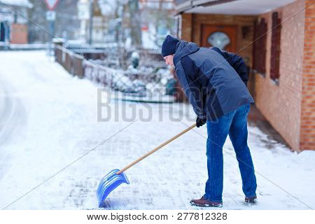 Man With Snow Shovel Cleans Sidewalks In Winter During Snowfall. Winter Time In Europe. Young Man In