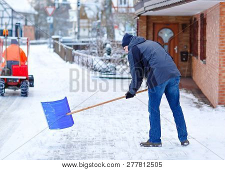 Man With Snow Shovel Cleans Sidewalks In Winter During Snowfall. Winter Time In Europe. Young Man In