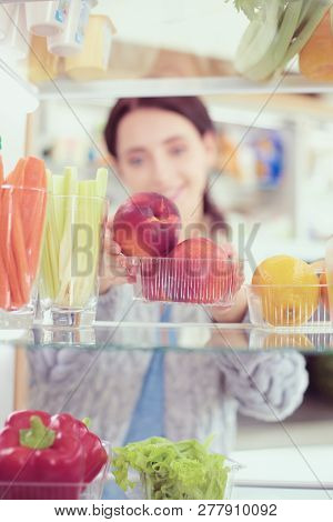 Portrait Of Female Standing Near Open Fridge Full Of Healthy Food, Vegetables And Fruits. Portrait O