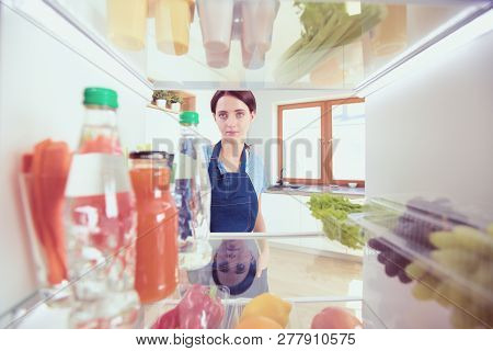 Portrait Of Female Standing Near Open Fridge Full Of Healthy Food, Vegetables And Fruits. Portrait O