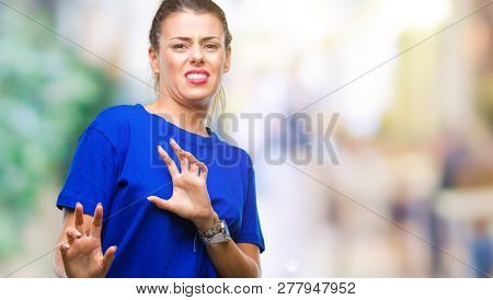 Young beautiful woman wearing casual blue t-shirt over isolated background disgusted expression, displeased and fearful doing disgust face because aversion reaction. With hands raised. Annoying
