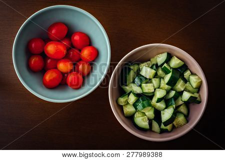 Ceramic Bowls Of Cherry Tomatoes And Cucumber Over A Wooden Table
