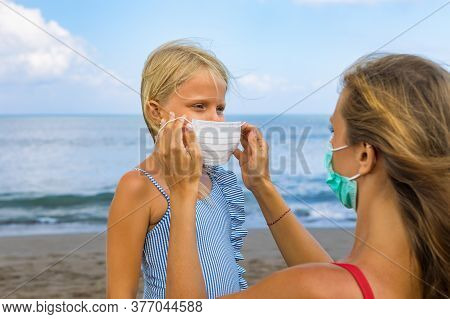 Mother Put Medical Mask On Child On Sea Beach. New Rules To Wear Cloth Face Covering At Public Place
