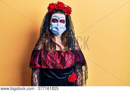 Young woman wearing day of the dead costume wearing medical mask looking positive and happy standing and smiling with a confident smile showing teeth 