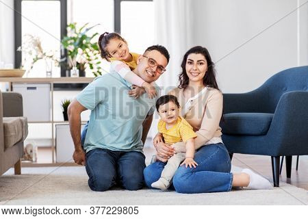 family and people concept - portrait of happy mother, father, little daughter and baby son sitting on sofa at home