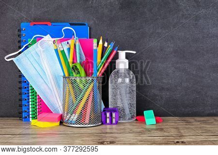 School Supplies And Covid 19 Prevention Items On A Desk Against A Chalkboard Background. Back To Sch