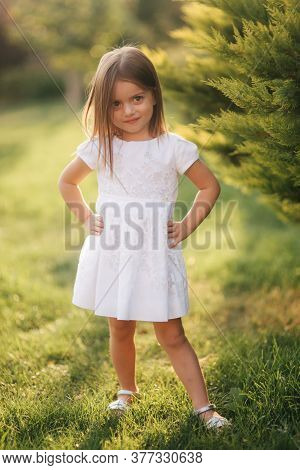 Beautiful Little Girl In White Dress Walking Outdoors On Back Yaer Of Home. Happy Kid