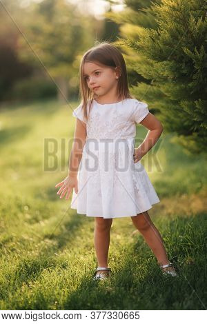 Beautiful Little Girl In White Dress Walking Outdoors On Back Yaer Of Home. Happy Kid
