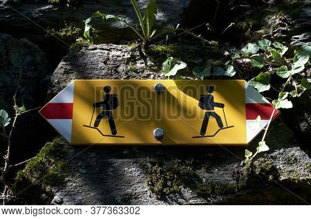 Close Up Of A Swiss Hiking Trail Direction Sign Illuminated By The Sun And Hanging On A Stone Wall A