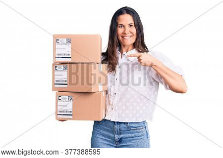 Young beautiful brunette woman holding delivery cardboard package pointing finger to one self smiling happy and proud 