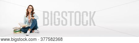 Portrait of a pretty casual girl student reading books while sitting on a floor books isolated over white background