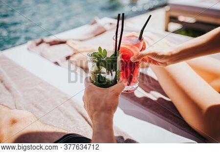 Young Hot Couple Resting At Swimpool. Picture Of Mans And Womans Hands Holding Cocktails. Cool Drink