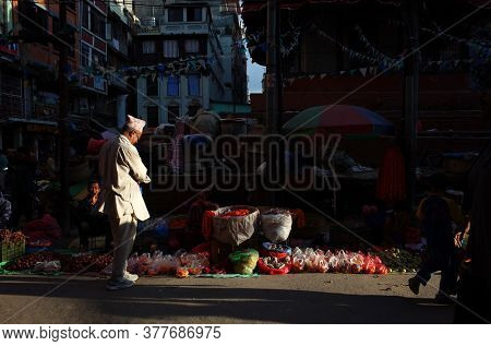 Kathmandu, Nepal - June 20, 2019: Sun shining on nepali man in traditional clothes on narrow shopping street in old town, Local daily life