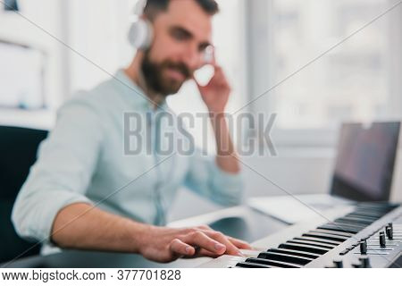Handsome Bearded Smiling Man Sits In Music Studio Composing Music On Keyboard Piano With Earphones O