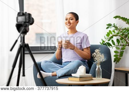 blogging, videoblog and people concept - happy smiling african american female video blogger with camera and cup of coffee videoblogging at home