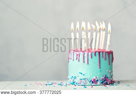 Birthday cake with blue frosting, pink drip icing and ten white birthday candles