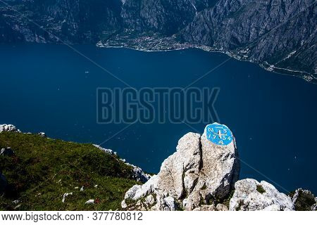 View Of Lake Garda And The Village Of Limone Between Rocks, Clouds And Blue Sky On Monte Altissimo D