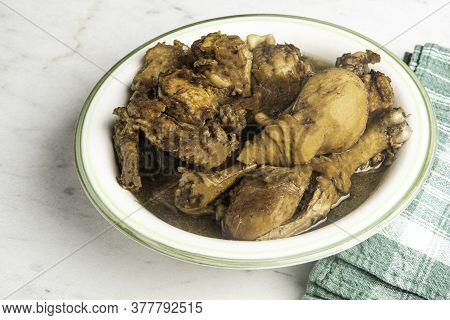 A Serving Of Filipino-style Chicken Adobo Dish In A Bowl With Green Napkin Set On A Marble Tabletop.
