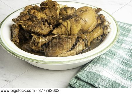 A Serving Of Filipino-style Chicken Adobo Dish In A Bowl With Green Napkin Set On A Marble Tabletop.
