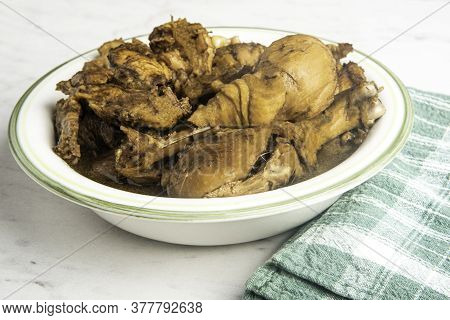 A Serving Of Filipino-style Chicken Adobo Dish In A Bowl With Green Napkin Set On A Marble Tabletop.
