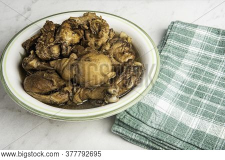 A Serving Of Filipino-style Chicken Adobo Dish In A Bowl With Green Napkin Set On A Marble Tabletop.
