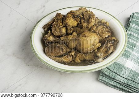 A Serving Of Filipino-style Chicken Adobo Dish In A Bowl With Green Napkin Set On A Marble Tabletop.