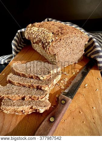 Loaf Of German Traditional Multi-cereal Bread Vollkornbrot, Partially Cut Into Slices On A Wooden Cu