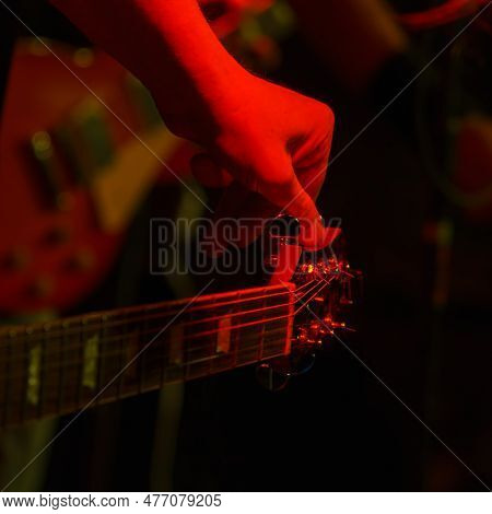 The Guitarist Tunes The Guitar Holding On To The Peg In The Spotlight. Guitar Tuning