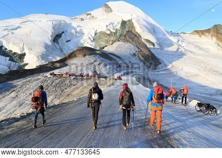 Group Of Mountaineers With Crampons On Ski Slope Ascending Towards Mountain Allalinhorn And Snow Mou