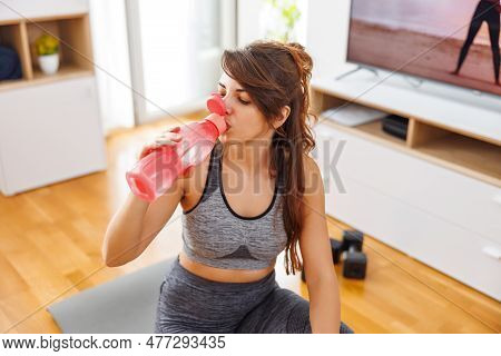 Active Young Woman In Sportswear Taking A Break While Doing Online Home Workout Session, Drinking Wa