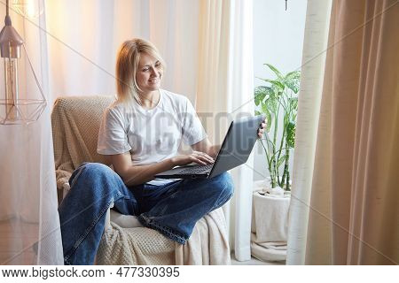 Young Blonde Woman Using Laptop Computer At Home. Girl Is Resting, Chating And Looking In Camera Nea