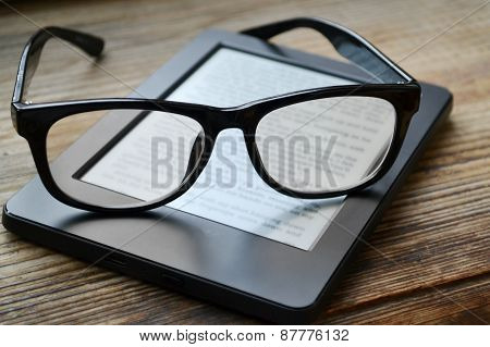 Black ereader with retro glasses on wooden table