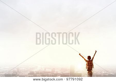Rear view of girl with hands up facing sunrise abone city