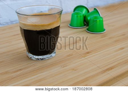 Close up of tasty espresso with foam and green coffee capsules on wooden background.Copy space.