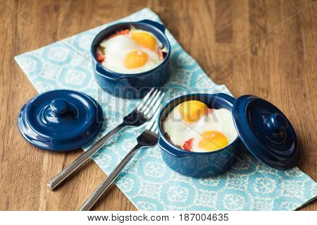 Baked eggs for breakfast in blue ceramic baking molds. Portioned casserole from vegetables and eggs in Italian style. Eggs Kokot