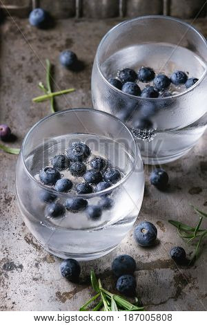 Tonic water cocktail with rosemary, blueberries. Two cold glasses over over dark texture metal background. Refreshing beverage alco non alcohol