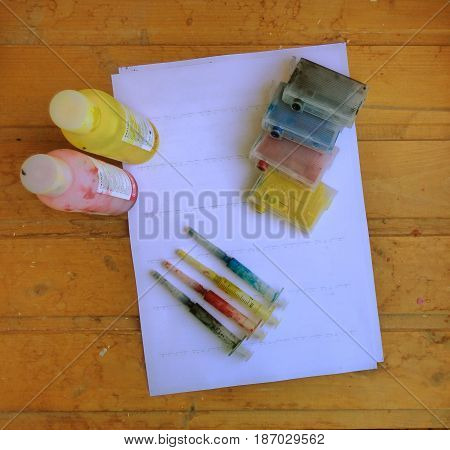 Set of Ink cartridges, refill paints in bottles and dirty syringes. On white paper. Jet printer maintenance.