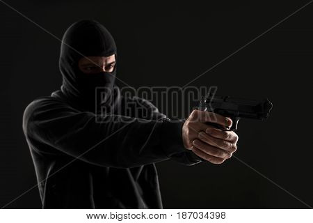 The robber in a mask with a gun pointed to the side on a black background. Man with a gun