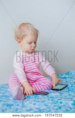 Cute adorable white Caucasian blond baby making a call playing with mobile cell phone with funny expression on face lifestyle new generation technology early development