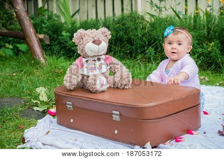 Baby sitting near suitcase in the summer garden