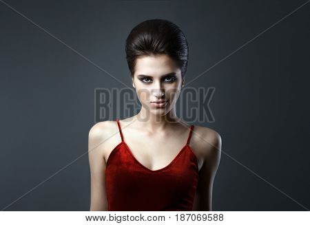 Beautiful woman with evening make-up and updo. Fashion photo. Girl wearing red dress ower dark background. Studio shoot.