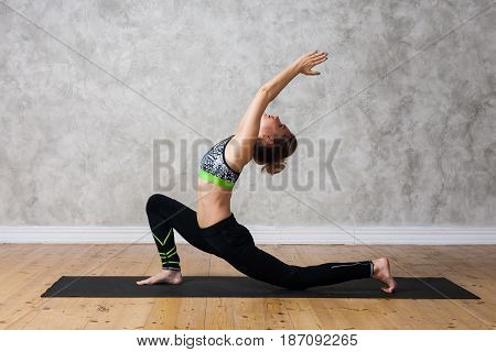 Young Woman Practicing Yoga Low Lunge Pose, Urdhva Ashva Sanchalasana  Against Texturized Wall / Urb