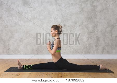 Young Woman Practicing Yoga Monkey King Pose, Hanumanasana Against Texturized Wall / Urban Backgroun