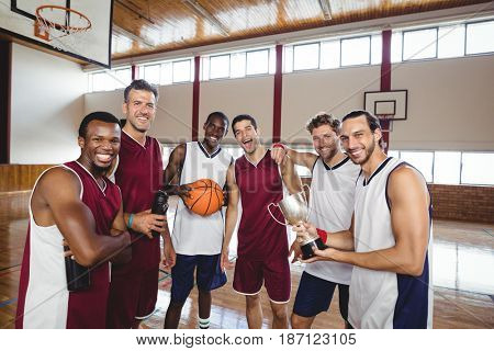 Portrait of smiling basketball players standing with throphy in the court