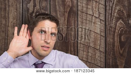 Digital composite of Businessman with hand on ear listening over wooden wall