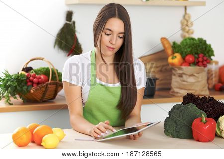 Young woman is making online shopping by tablet computer and credit card. Housewife found new recipe for cooking in a kitchen.