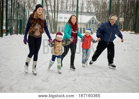 Family of five skates holdind hands at outdoor rink on winter day.